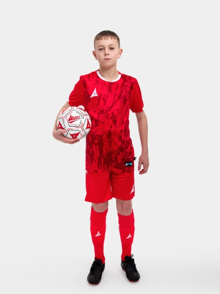 	A young child is wearing a red Football Shirt. The football shirt has a camo pattern and matching red socks and shorts
