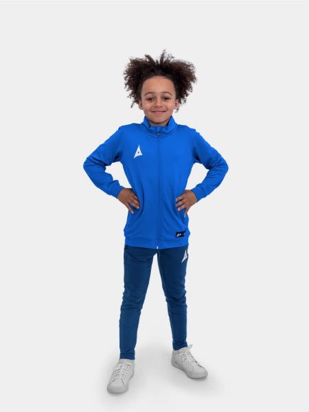 	There is a child wearing a Junior sized Jacket in Royal Blue and has matched it with Navy Jogging Bottoms.