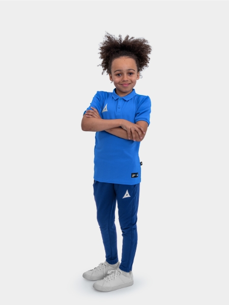 A boy is stood wearing the Avec Focus 2 Royal Tech Polo and the Avec Focus 2 Navy Track Pant