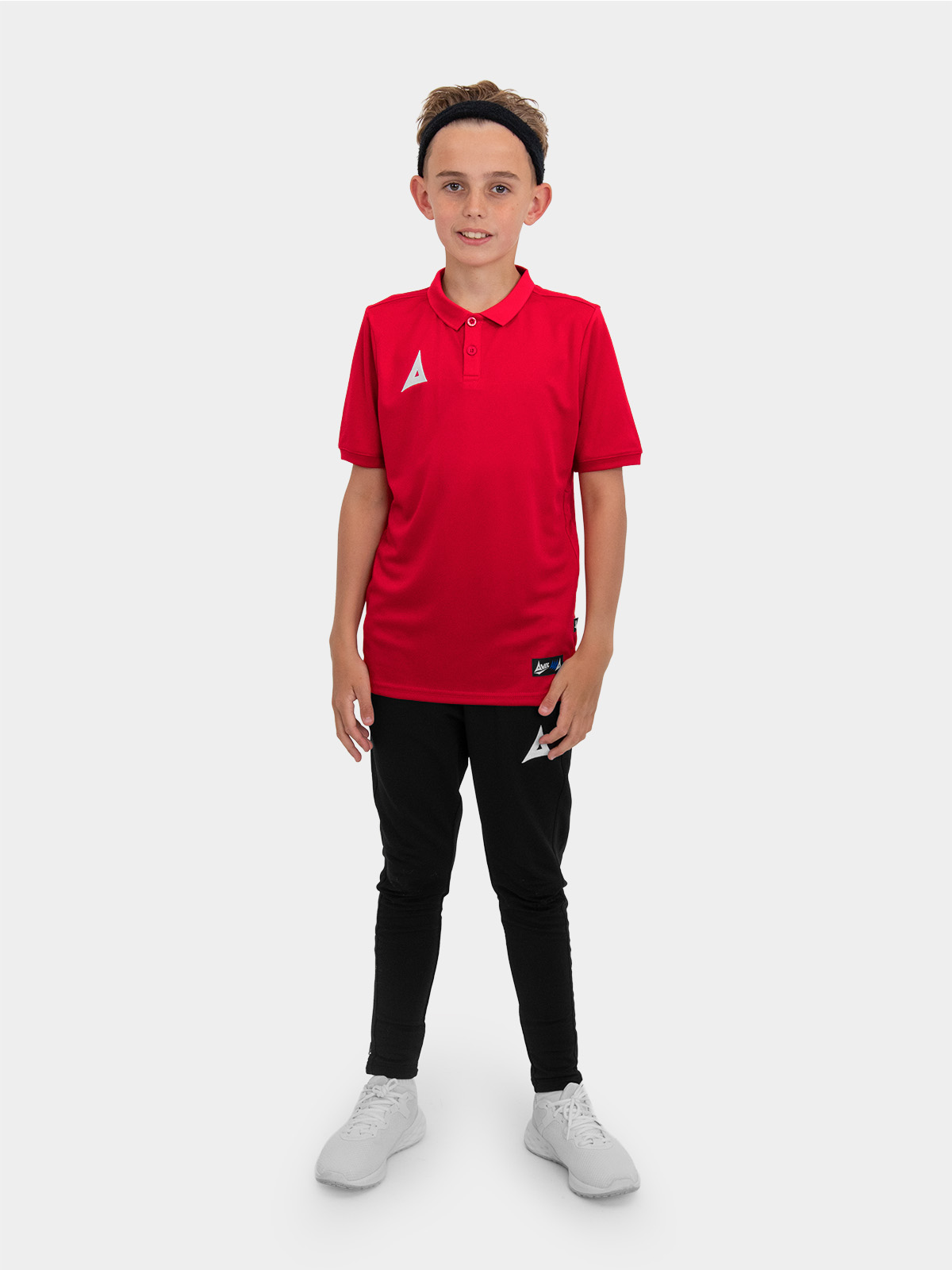 	a boy is stood wearing the avec focus 2 red tech polo and the avec focus 2 black track pant, smart polo and joggers for training