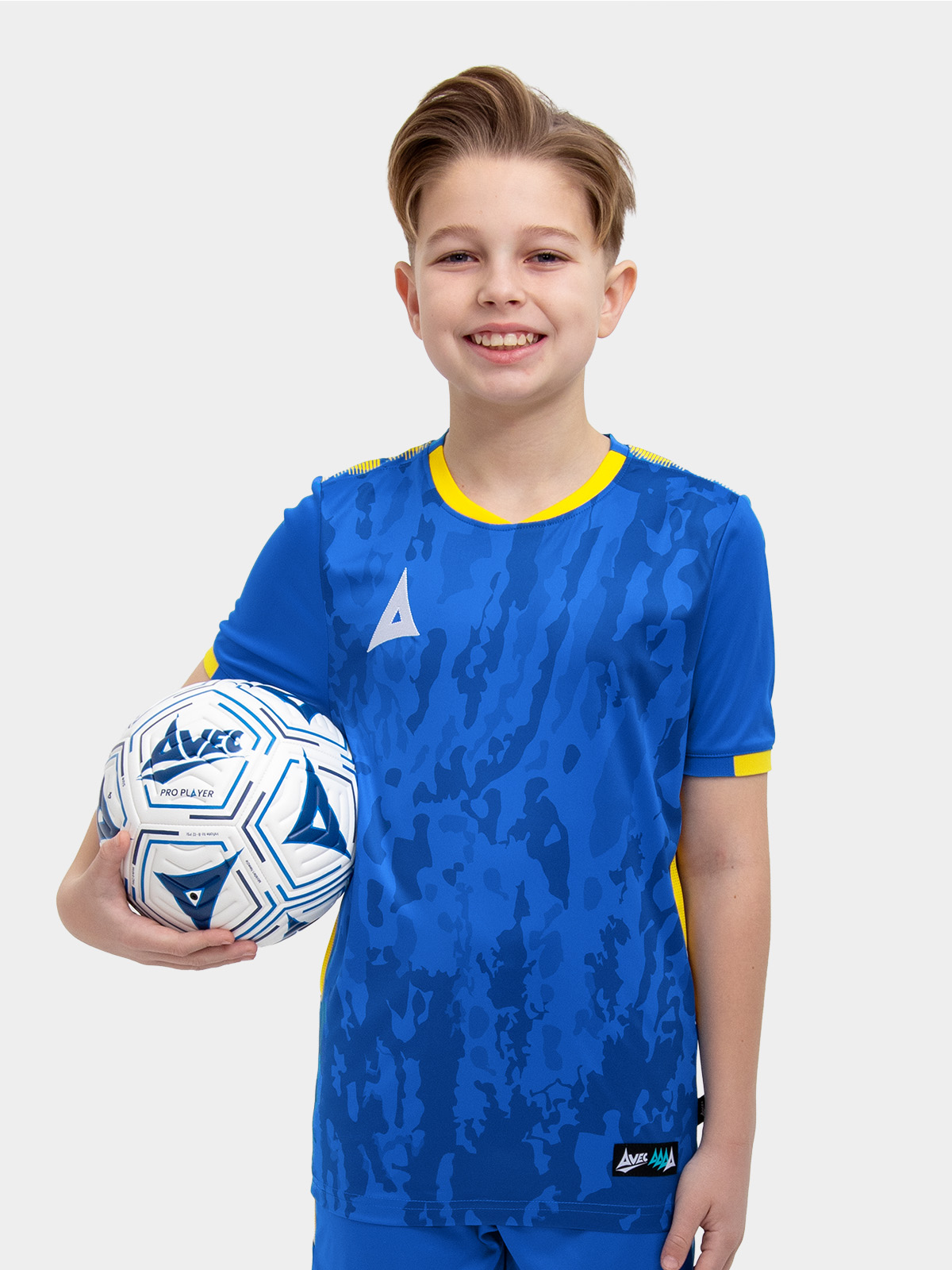	a kids football kit in royal blue and yellow with matching blue shorts and socks holding a football