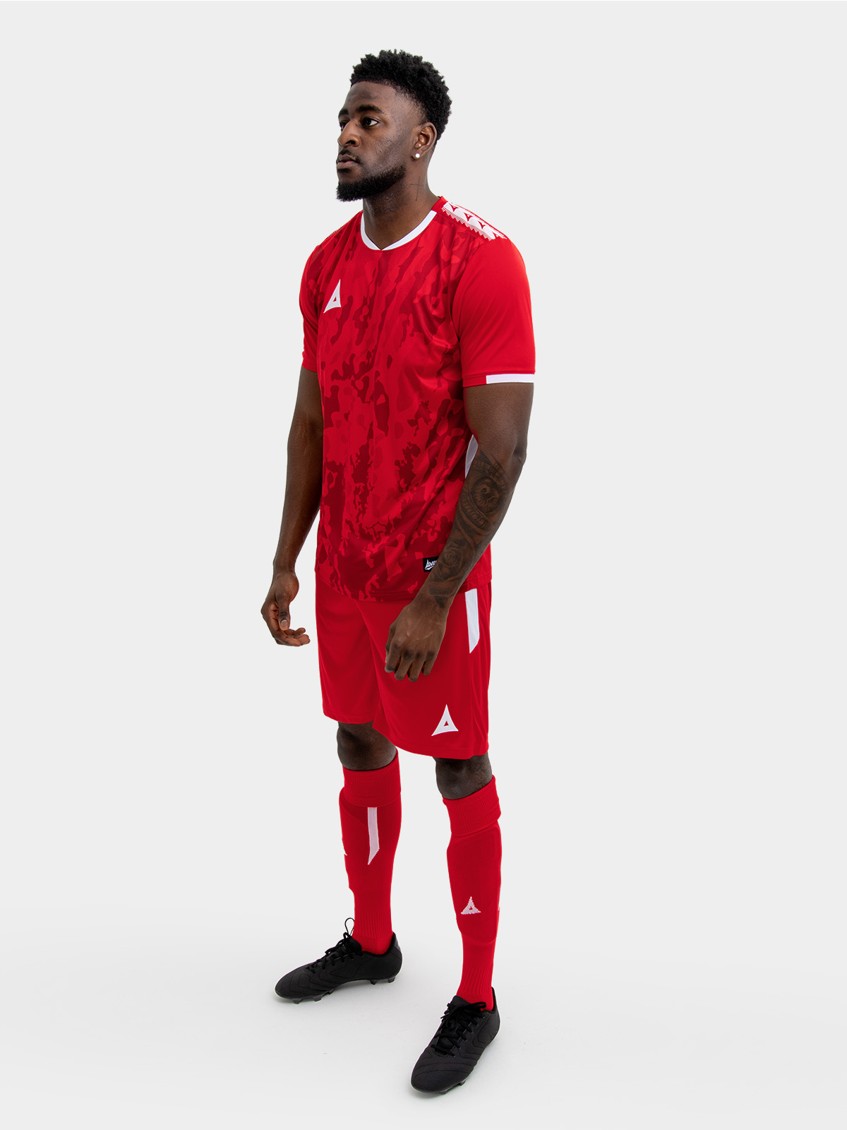 	a man standing up wearing a red football shirt, matching red shorts and red football socks.