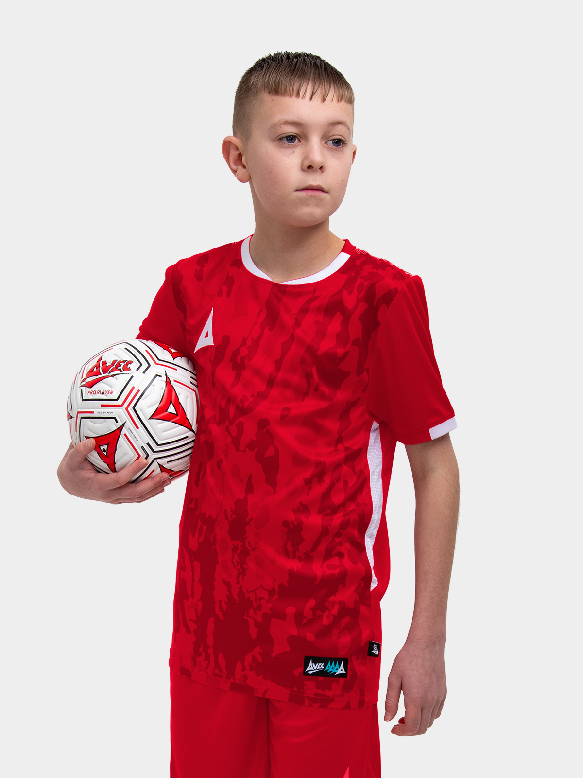 	a young kid standing up wearing a red football shirt holding a red football