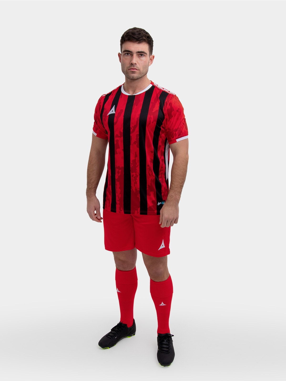 	a model standing up wearing a red and black football shirt, red shorts and red football socks.