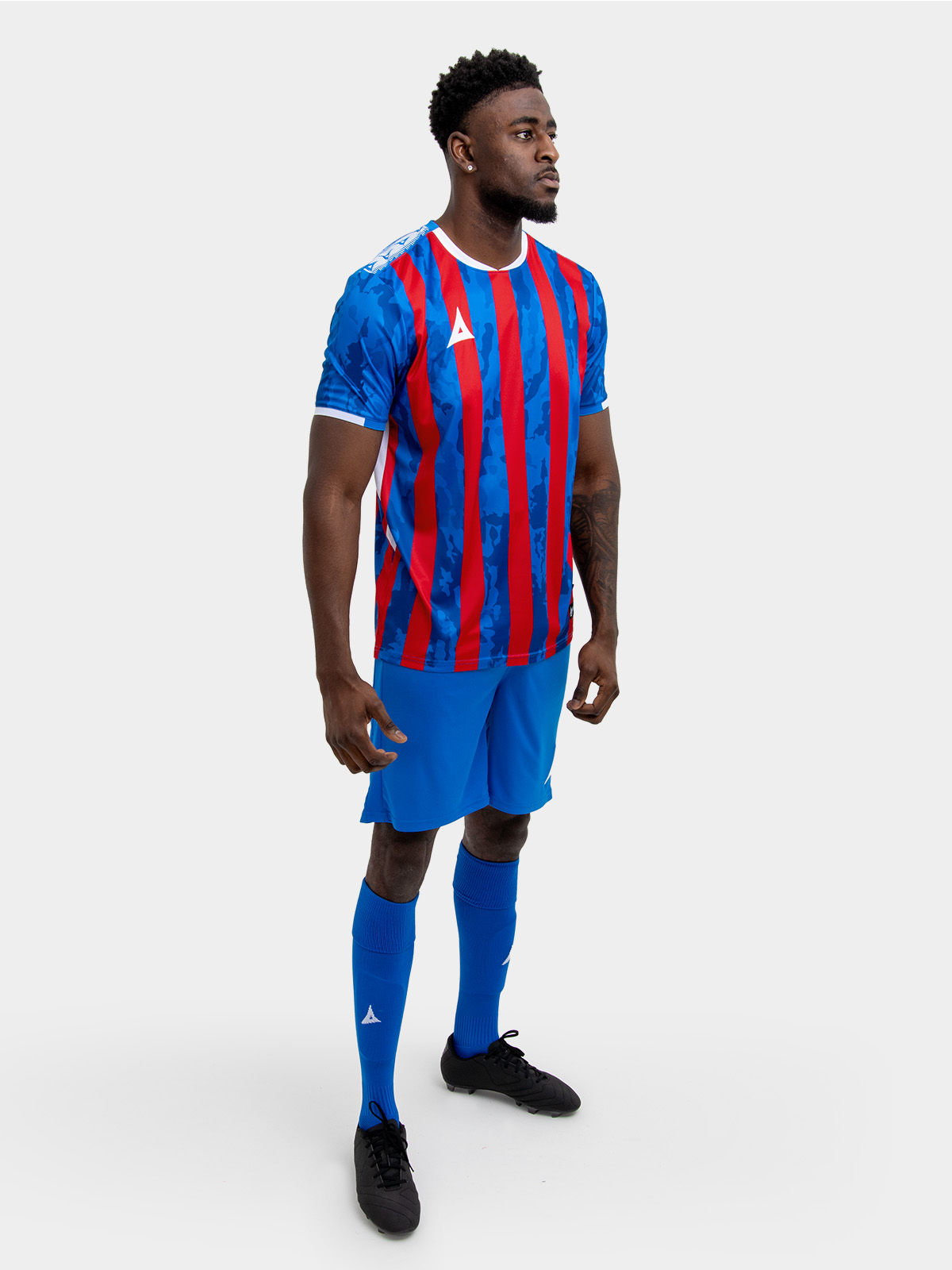 	a model standing up wearing a red and royal blue football shirt, blue shorts and blue football socks.