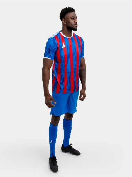 	A model standing up wearing a red and royal blue football shirt, blue Shorts and blue Football Socks.