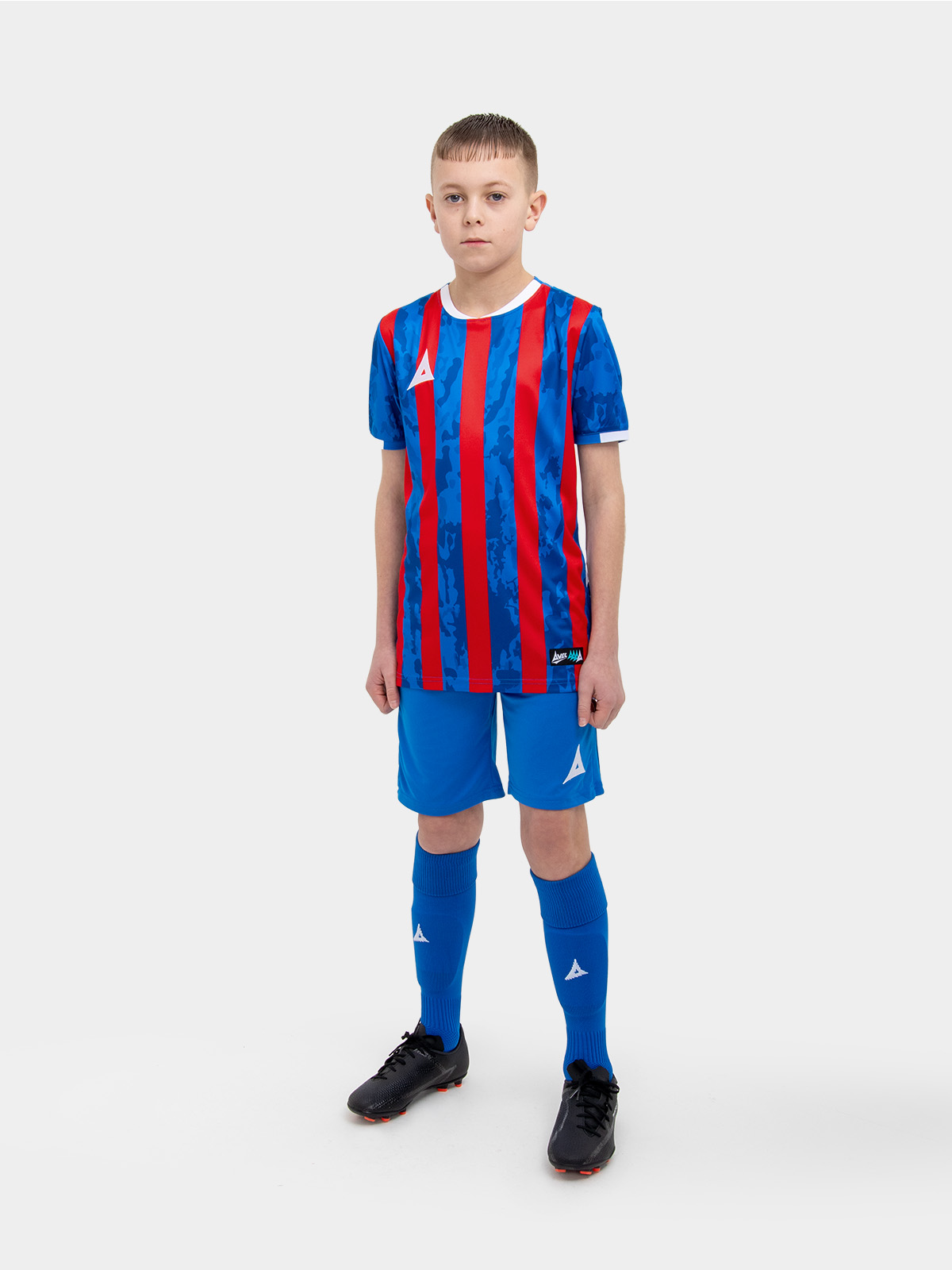 	a kid standing up wearing a red and royal blue football shirt and matching socks and shorts