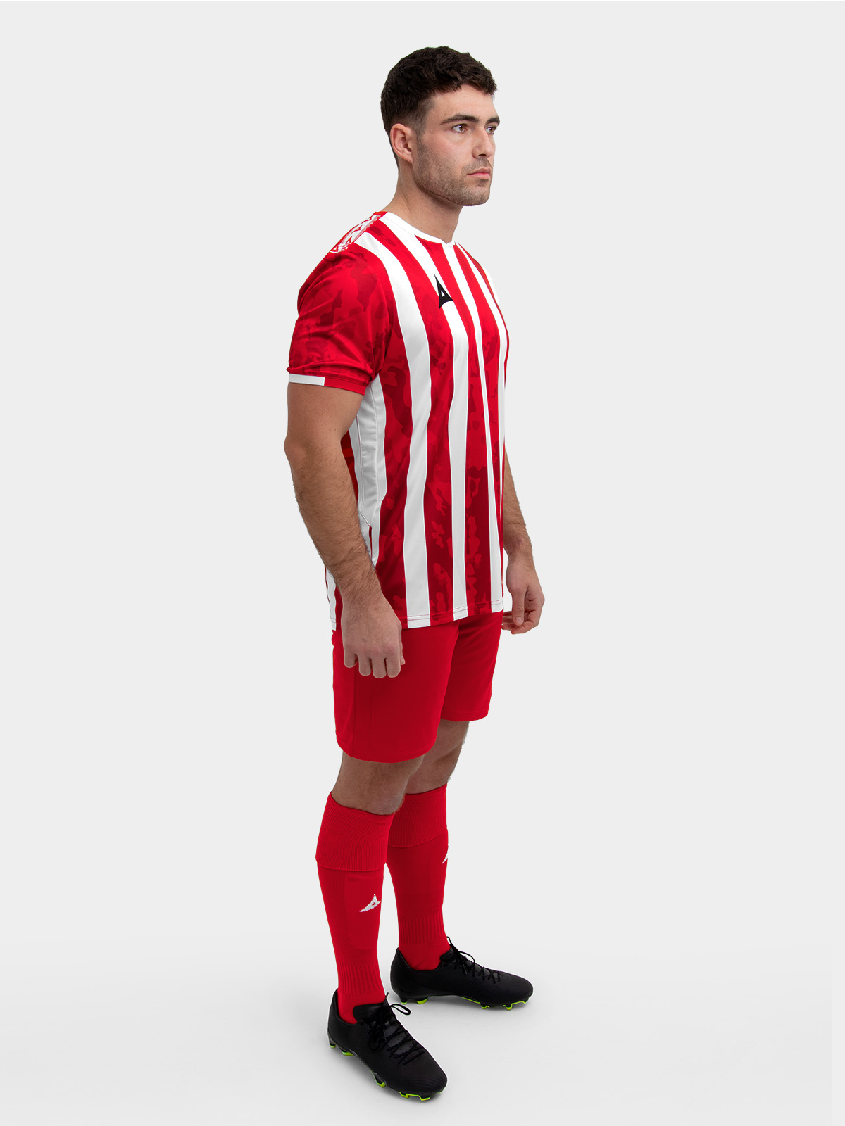 	a model standing up wearing a red and white football shirt, red shorts and red football socks.