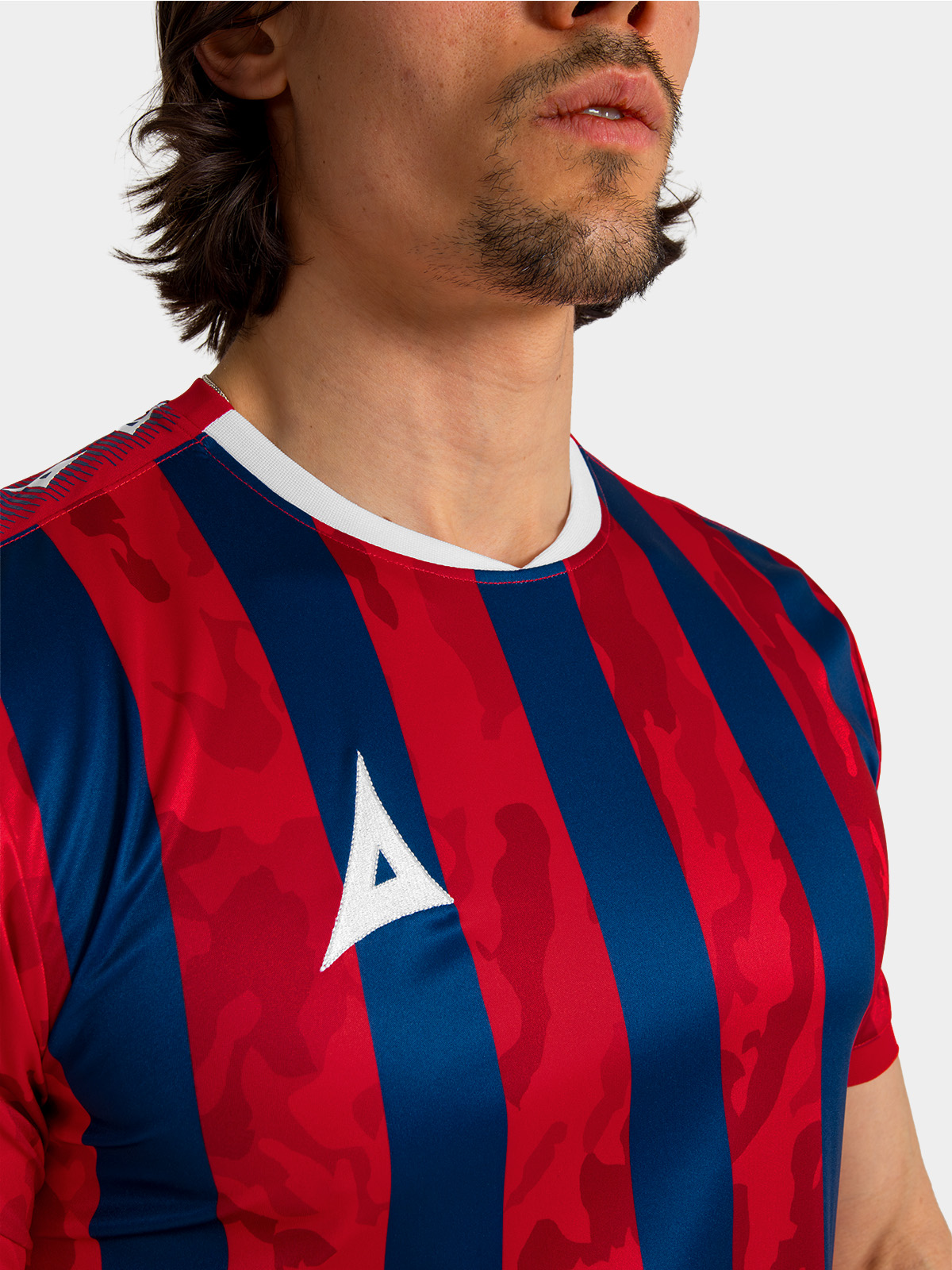 	detailed view of the embroidered avec logo and clean white trim on the red and navy camo-stripe jersey.	